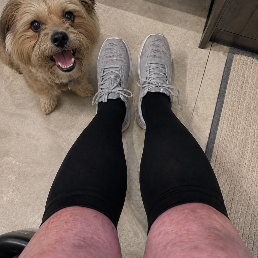 Gambe con calze a compressione nere Vitalis e un cagnolino sul pavimento